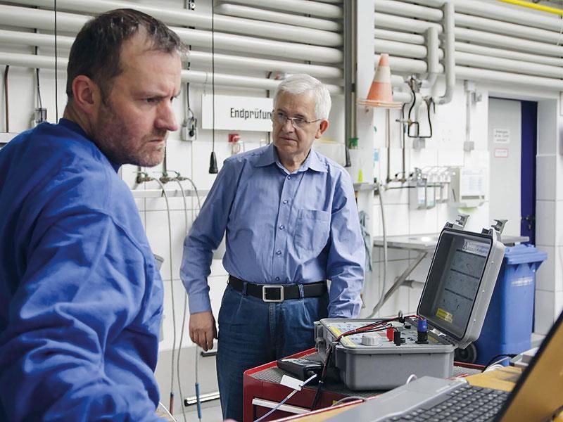 Zwei Männer arbeiten in einer Fabrik an einem Laptop.