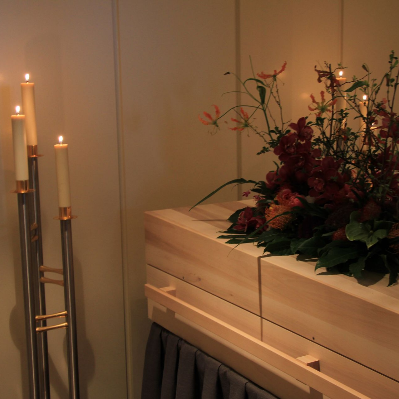 Cercueil en bois orné d’une composition florale, entouré de bougies allumées dans un cadre funéraire