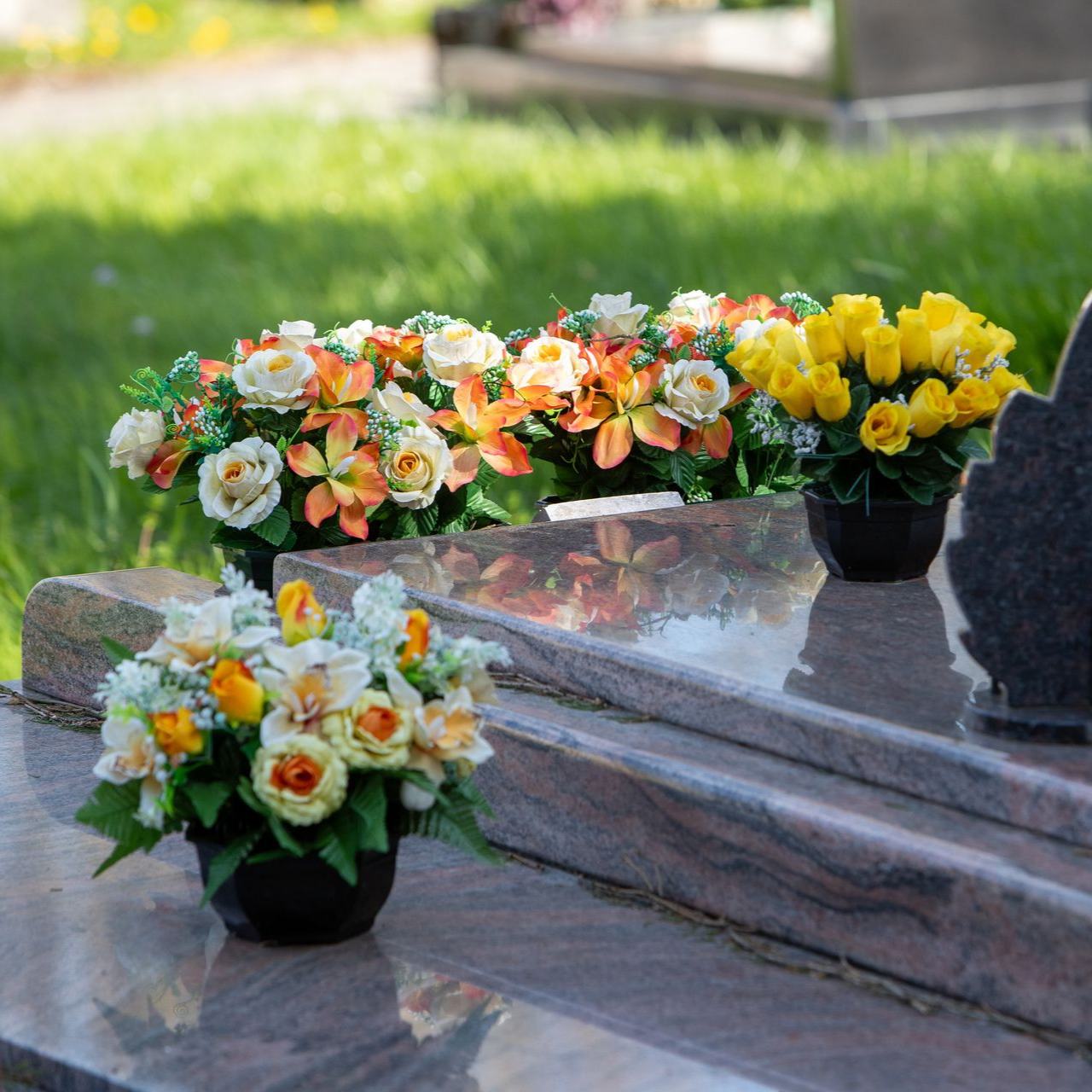 Compositions florales sur une marche en pierre à l’extérieur, avec des fleurs orange, blanches et jaunes dans des pots noirs