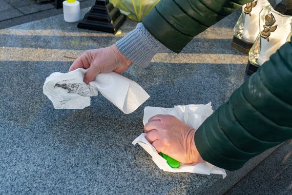 Des mains essuient une surface grise avec des chiffons blancs dans un cimetière