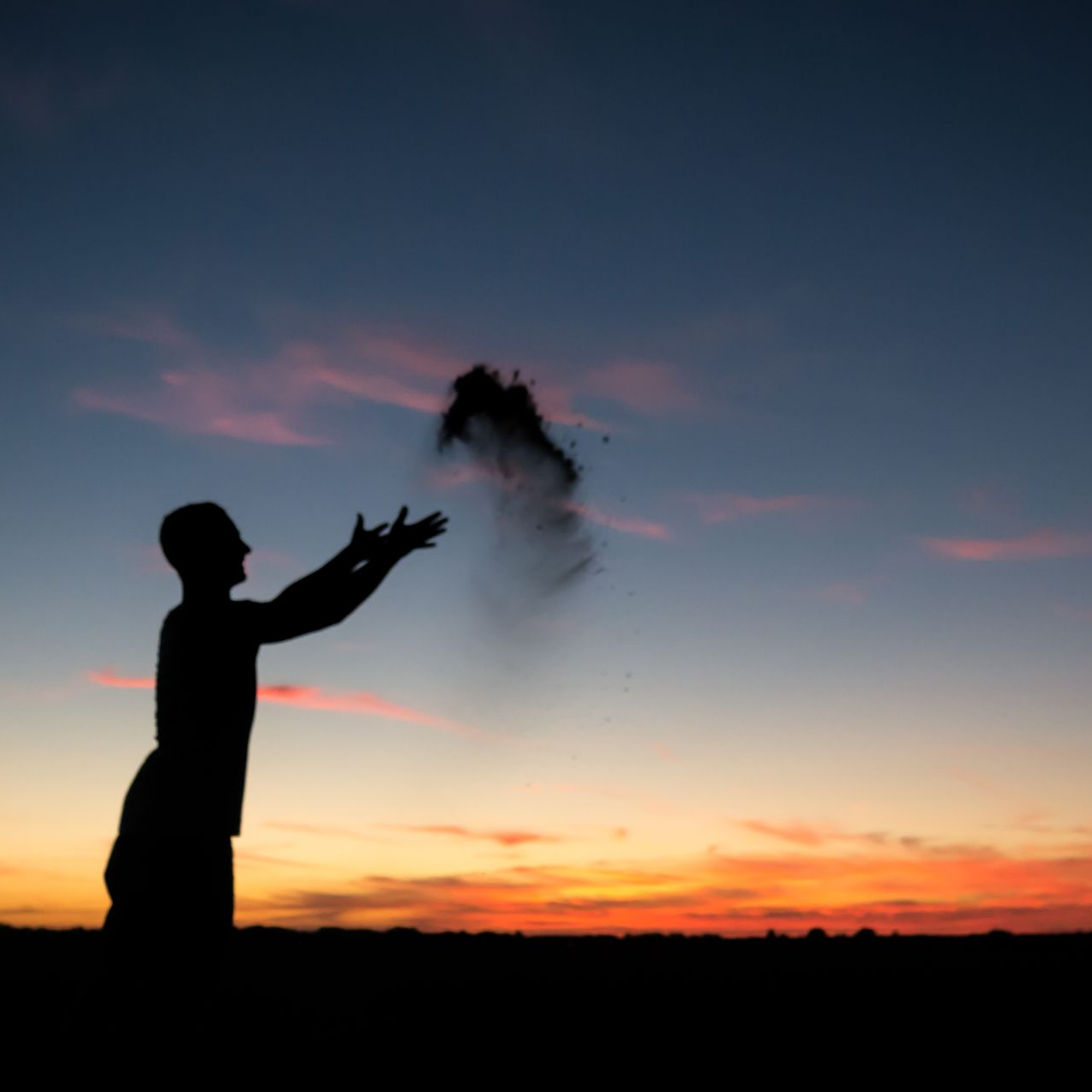 Silhouette d’une personne lançant une poignée de cendres au coucher du soleil