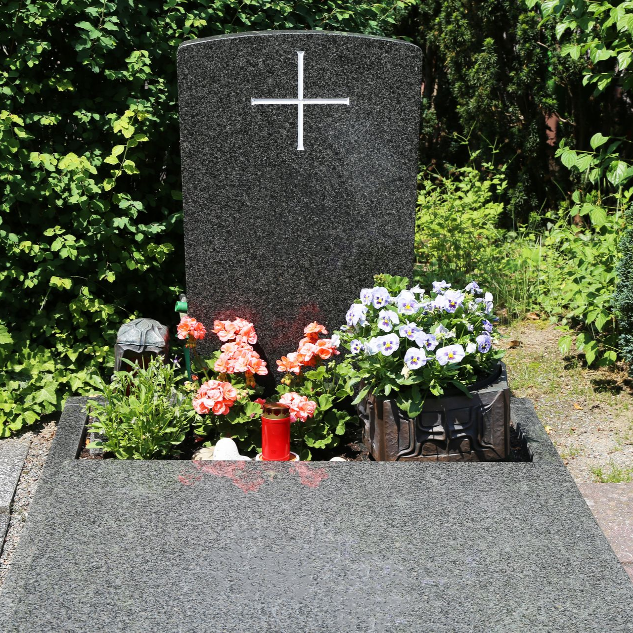 Pierre tombale avec une croix blanche, entourée de fleurs colorées dans un cimetière