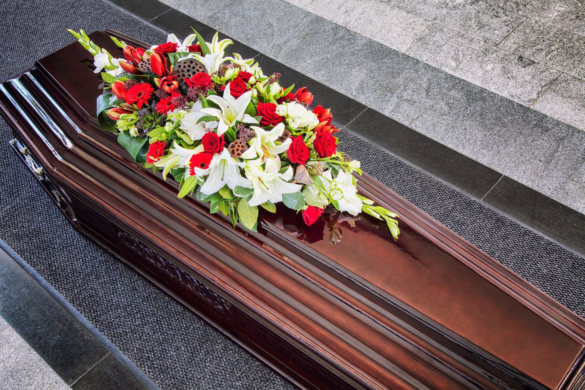 Cercueil fermé en bois avec des fleurs rouges et blanches posées dessus
