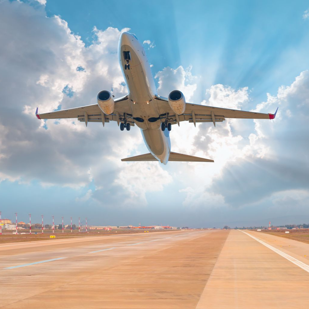 Un avion décolle au-dessus d’une piste sous un ciel bleu rempli de nuages