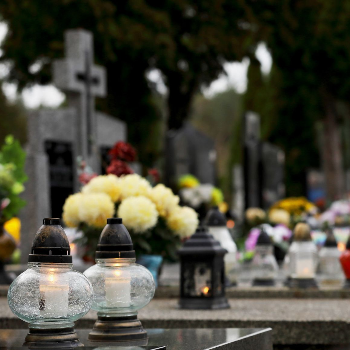 Cimetière commémoratif avec des lanternes allumées, des fleurs et des pierres tombales en arrière-plan
