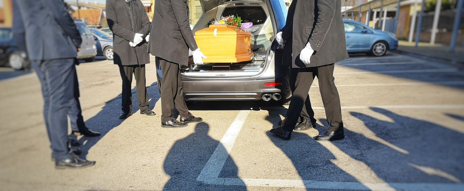 Des personnes rassemblées autour du coffre ouvert d’un corbillard, prêtes à porter un cercueil en bois