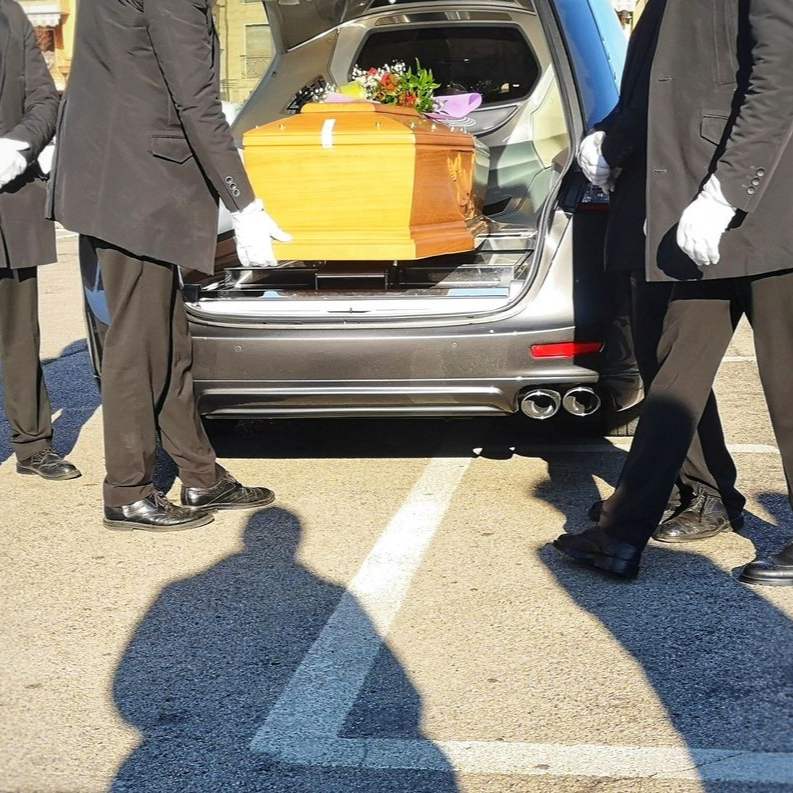 Cercueil fleuri dans un corbillard ouvert, avec des porteurs se tenant à côté, en plein air