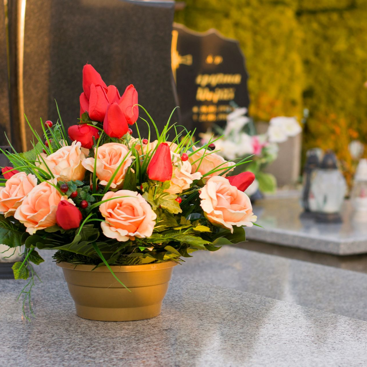 Des roses et des tulipes rouges dans un vase doré posé sur une surface en pierre dans un cimetière