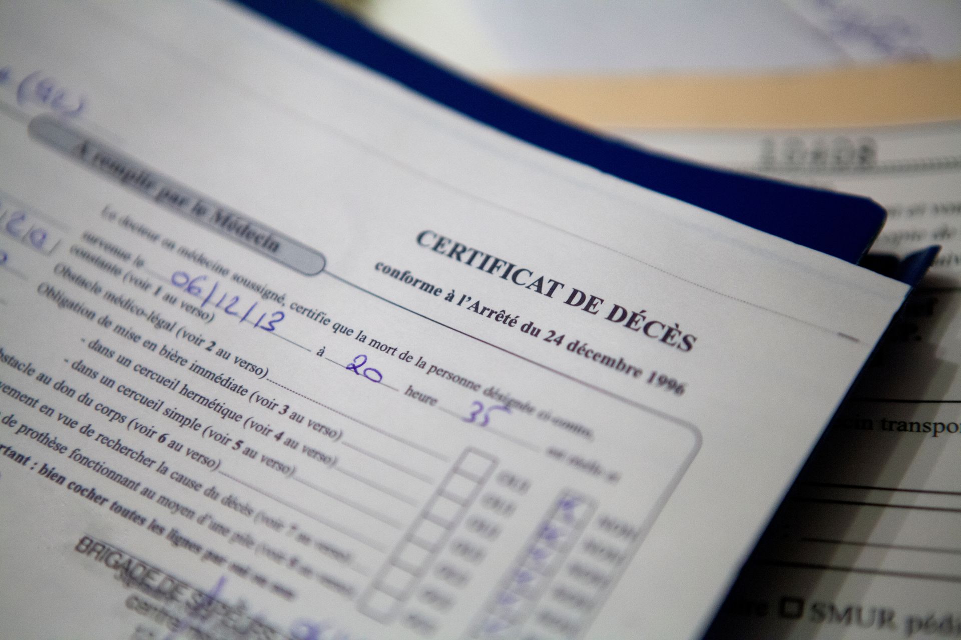 Formulaire français de certificat de décès posé sur un bureau, avec du texte imprimé et des annotations manuscrites en bleu