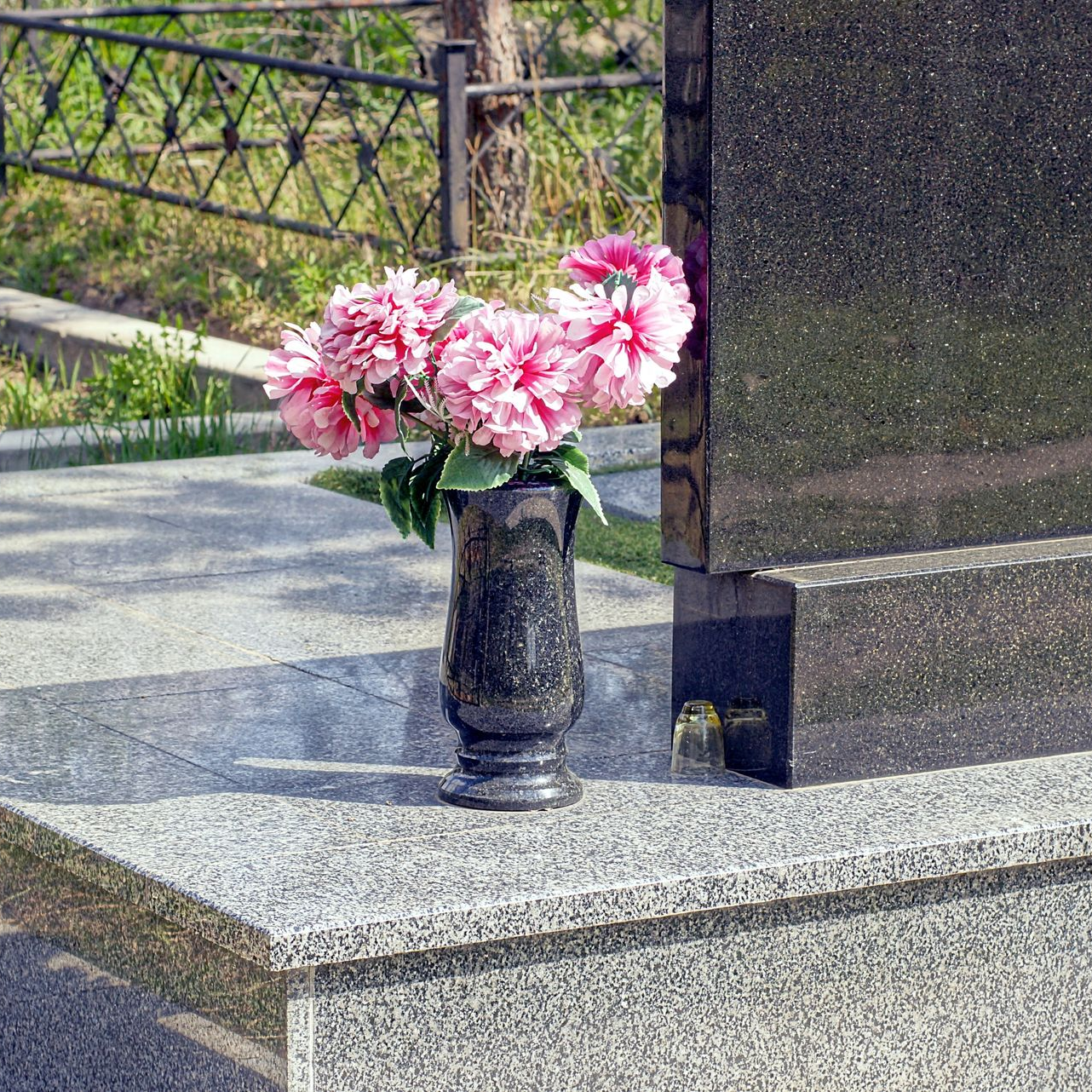 Vase de fleurs roses posé sur une corniche commémorative en granit, dans un cimetière