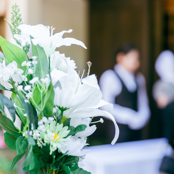 Composition florale blanche au premier plan, avec des personnes floues debout à l’intérieur en arrière-plan