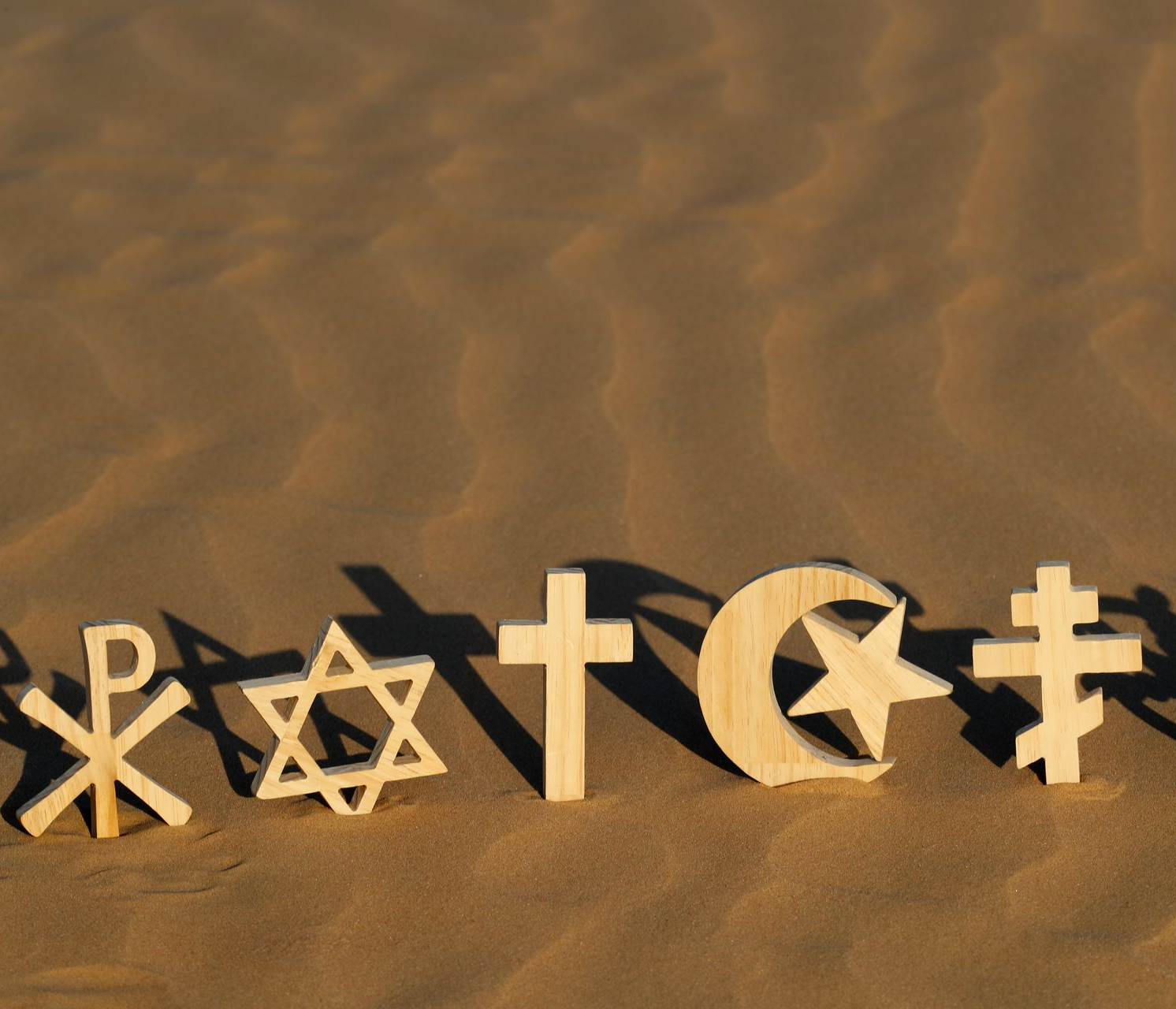 Symboles religieux disposés dans le sable, notamment une croix, une étoile de David, un croissant et d’autres signes religieux