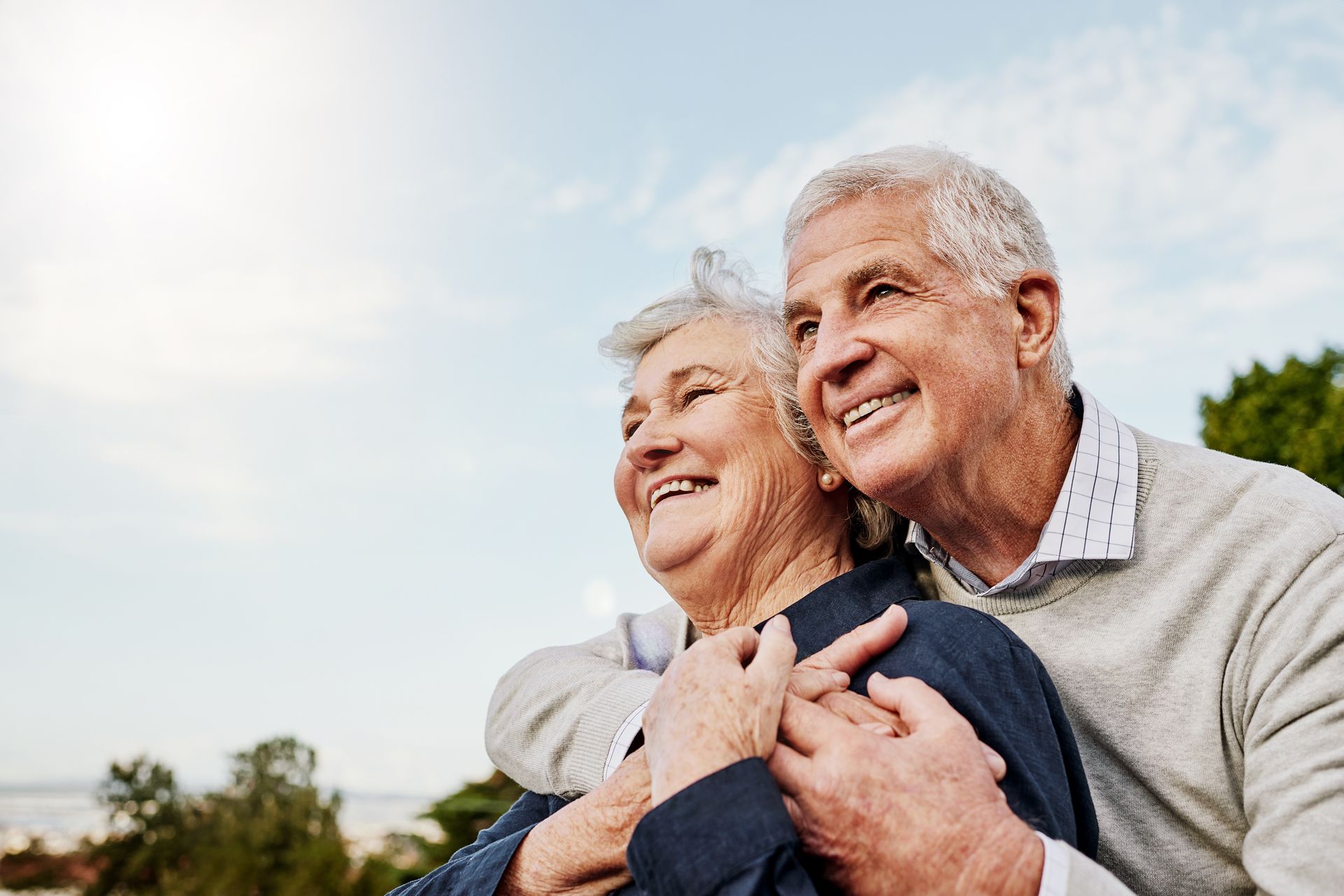 Un couple souriant qui s’enlace dans un parc ensoleillé, regardant au loin