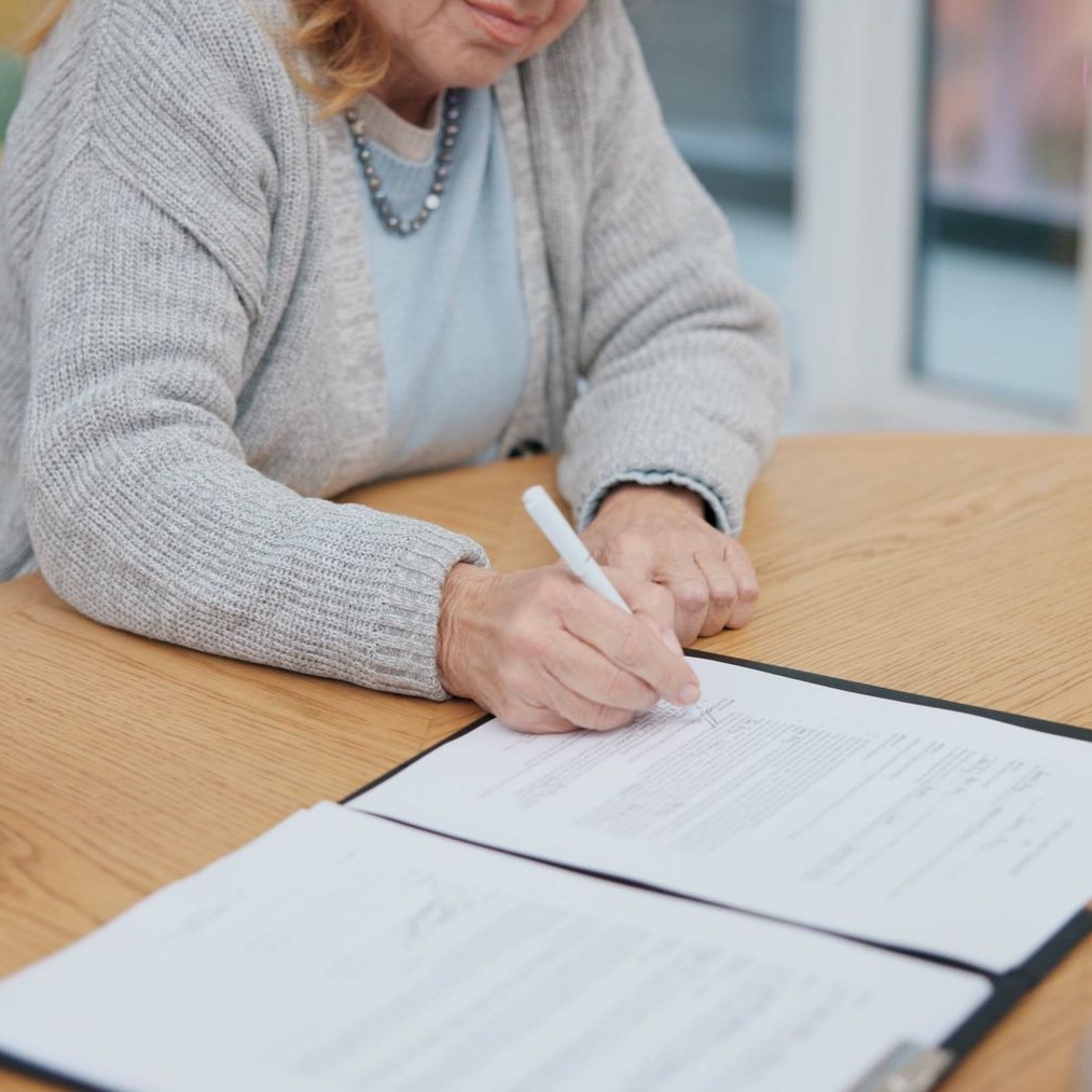 Personne en train de signer un document à une table en bois, avec des papiers étalés