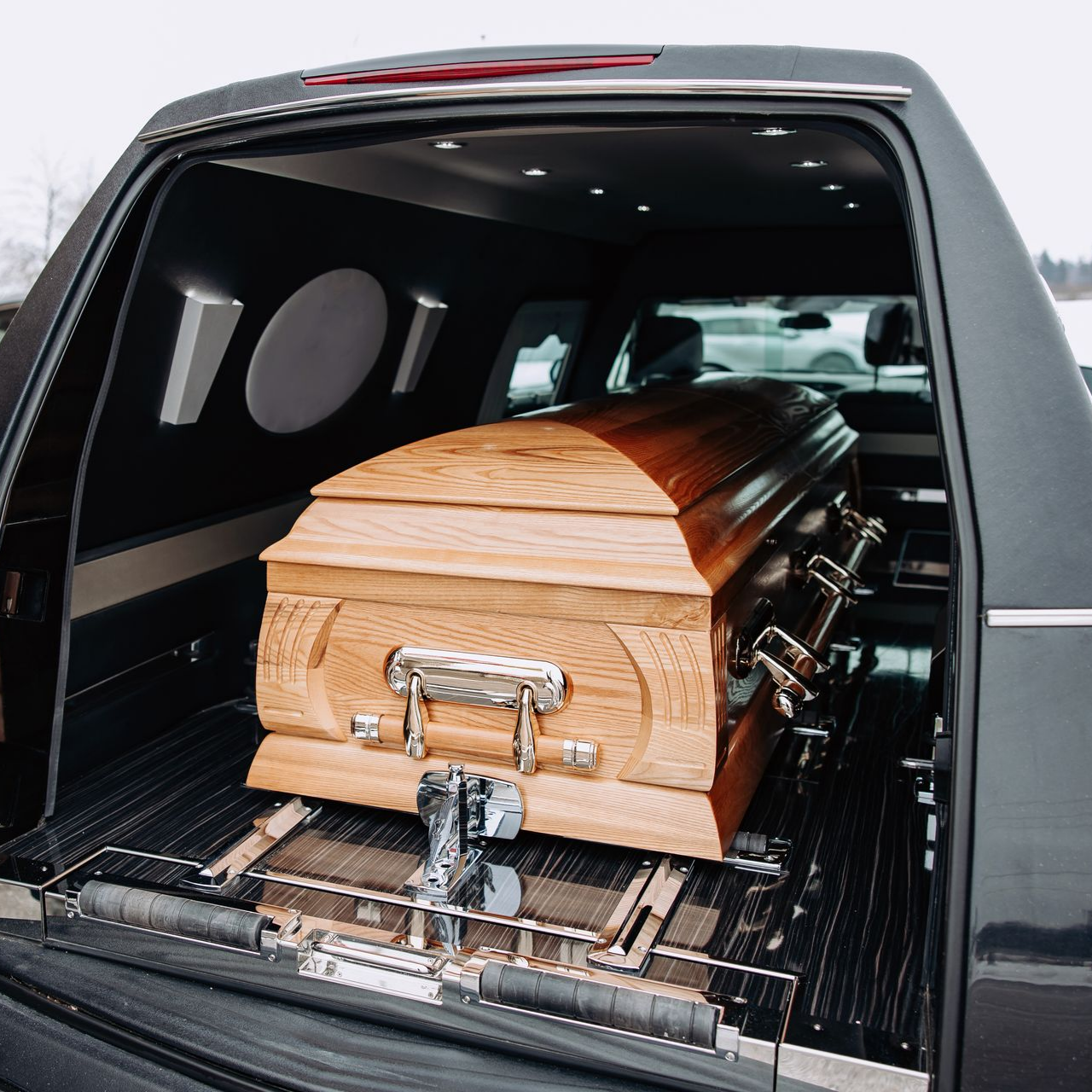 Cercueil en bois sanglé à l’intérieur du compartiment de chargement d’un véhicule noir de type corbillard