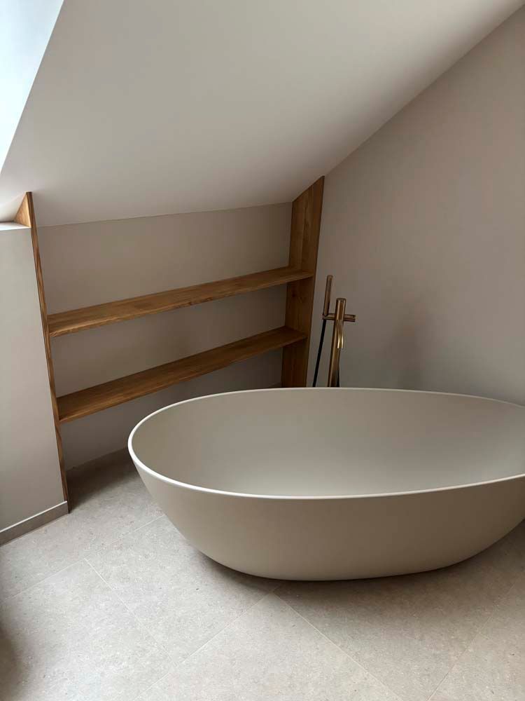 Eine große weiße Badewanne in einem Badezimmer neben einem Holzregal.