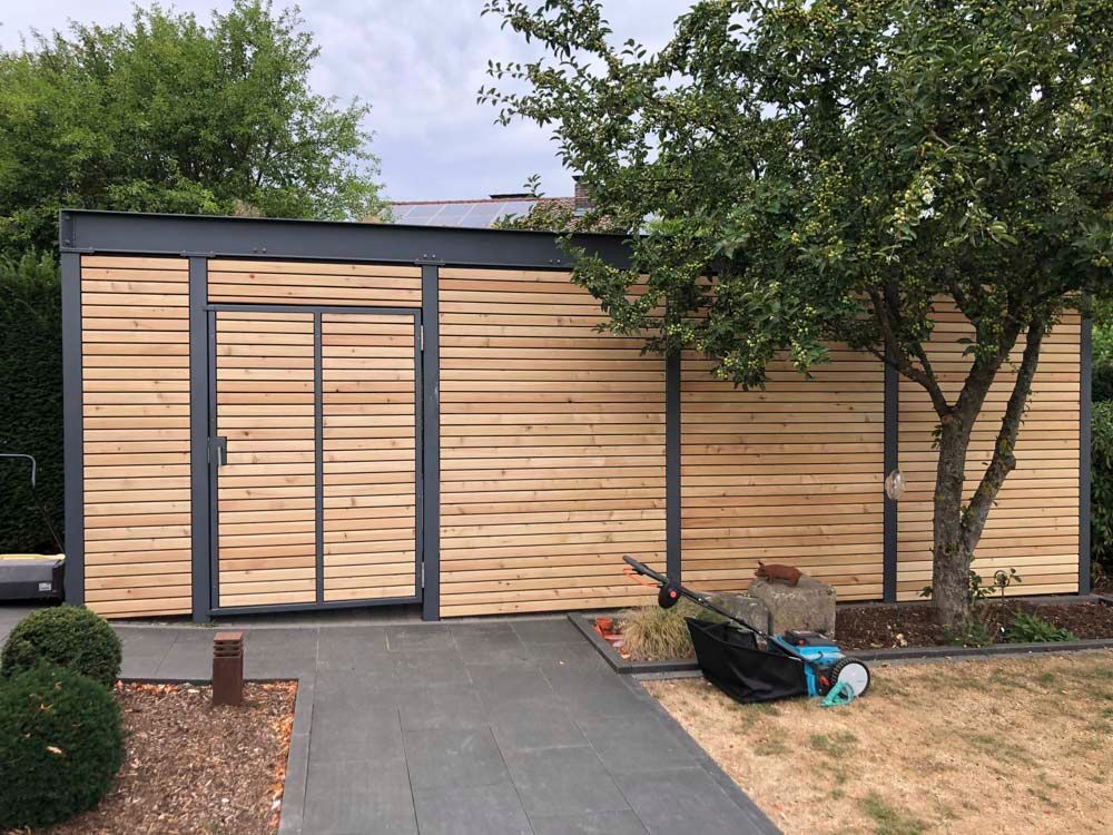 Ein Holzschuppen mit einer Tür und einem Baum davor.