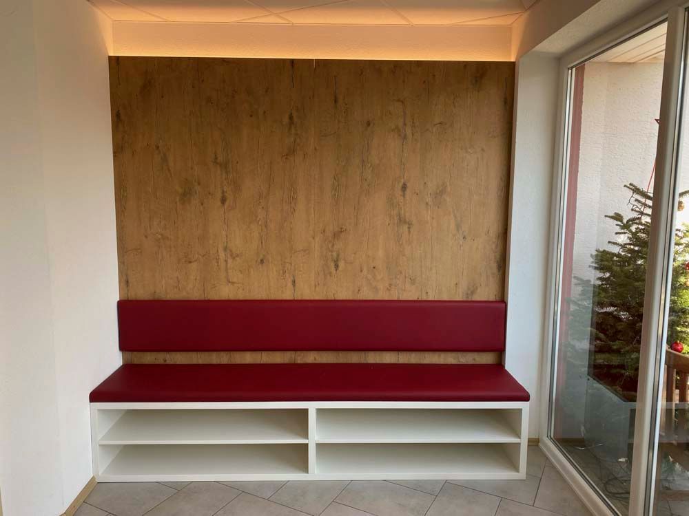 In der ecke des raumes steht eine bank mit einem roten kissen.