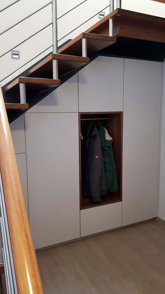 Ein Mantel hängt in einem Schrank unter einer Treppe.