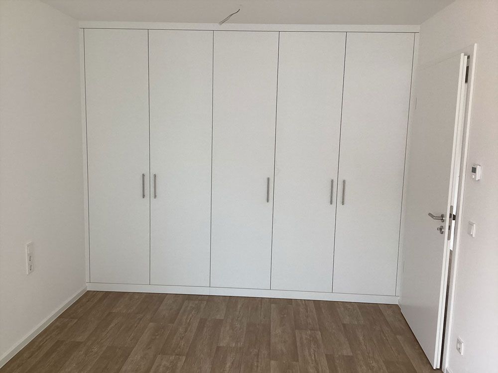 Leeres Zimmer mit weißen Einbauschränken, weißen Wänden und Holzboden