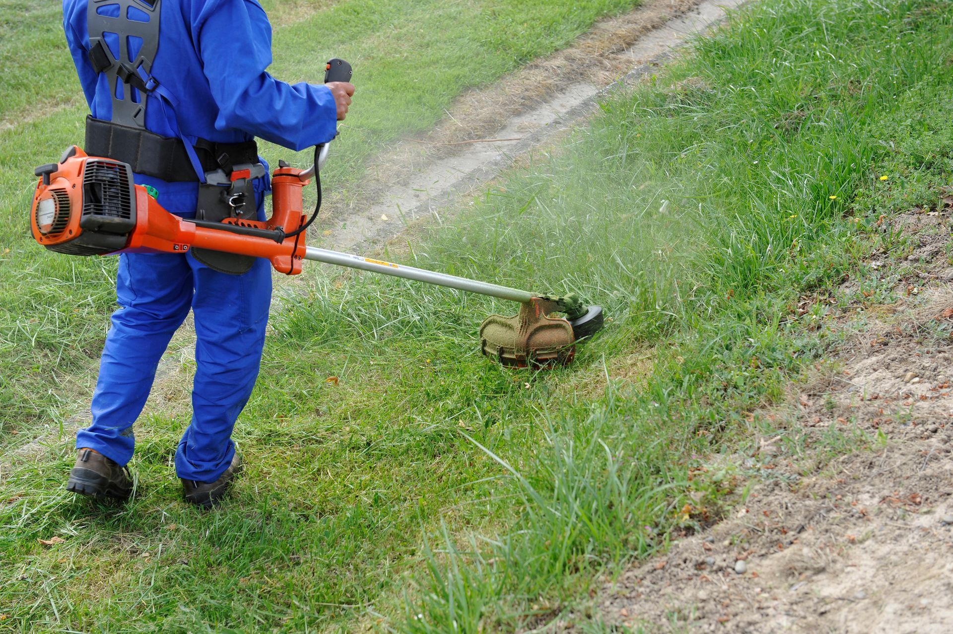 Une personne en salopette utilise une débroussailleuse pour tondre de l'herbe.