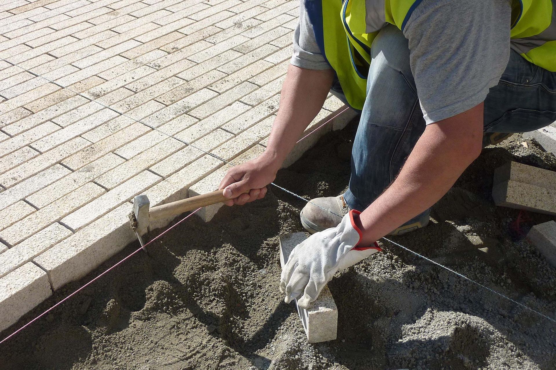 Un ouvrier applique du béton sur le bord d’un trottoir à l’aide d’une truelle et de ses mains gantées