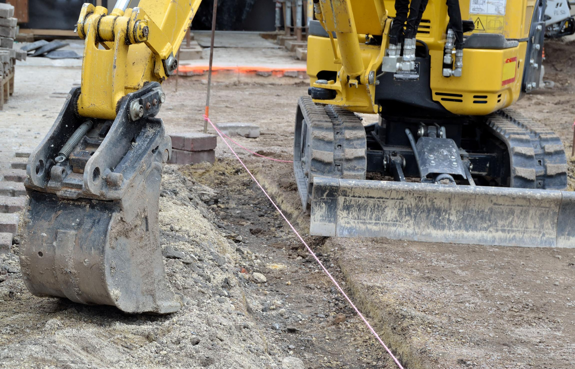 Deux excavatrices jaunes sur un terrain de chantier boueux, avec un godet au premier plan.