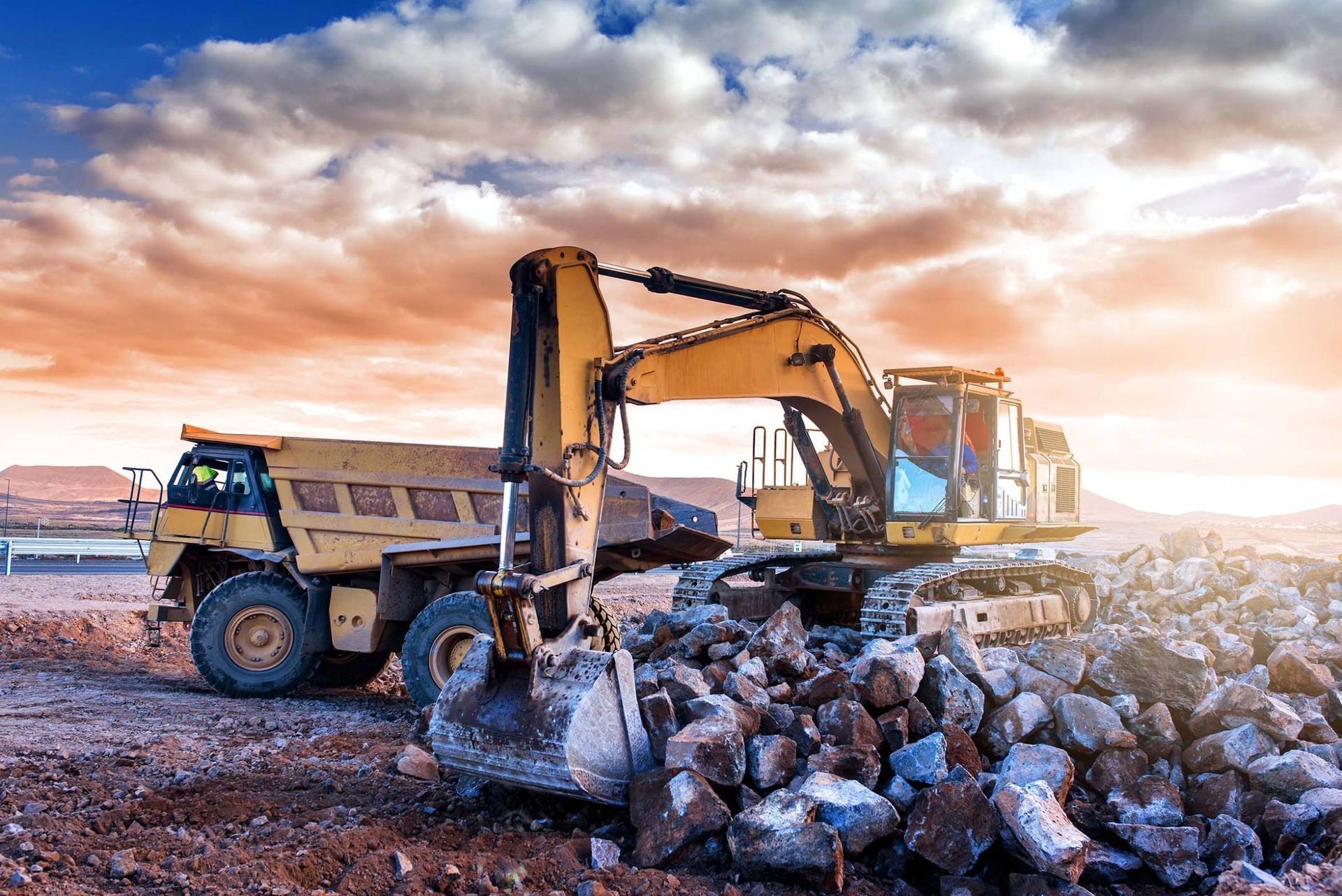 Une excavatrice charge des roches dans un camion-benne sur un chantier au coucher du soleil