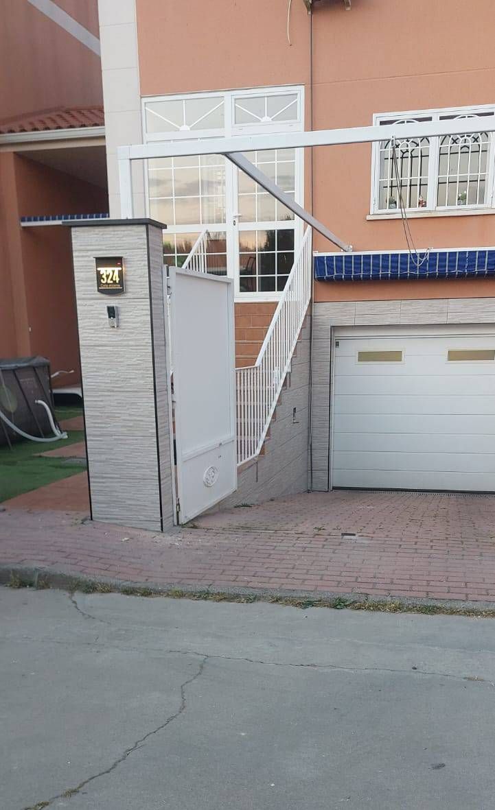 Casa naranja con portón blanco, garaje y pilar de ladrillo gris con placa de dirección.