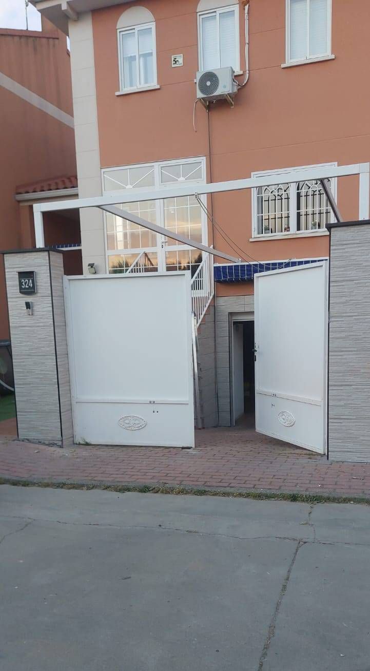Puerta blanca frente a un edificio naranja de dos pisos. Puerta abierta. Camino pavimentado.