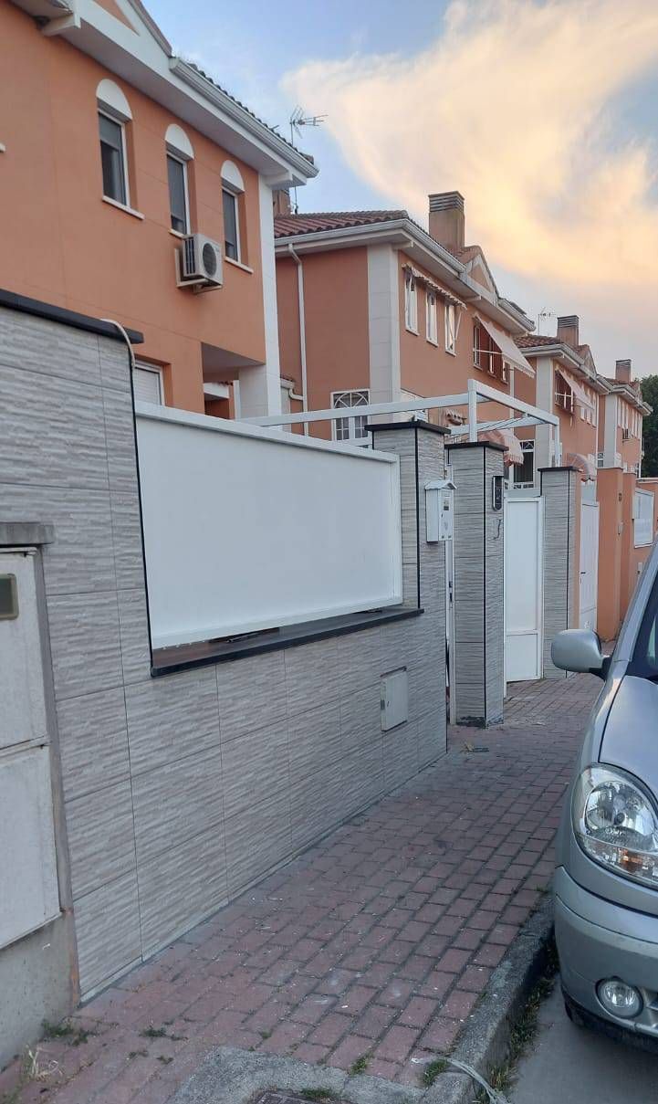 Hilera de casas adosadas de color naranja detrás de un muro de piedra gris con toldos blancos, una calle y un coche aparcado.