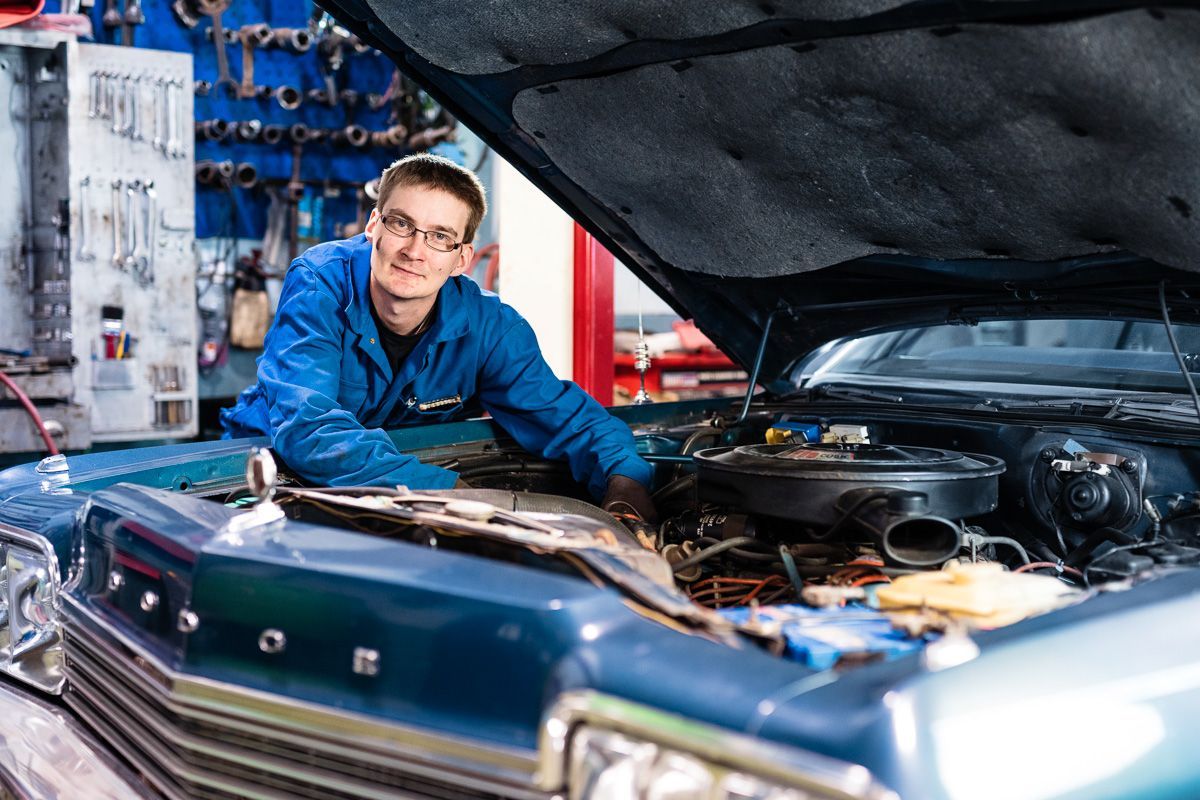 Mechanic in blue jacket working under a car hood in a garage