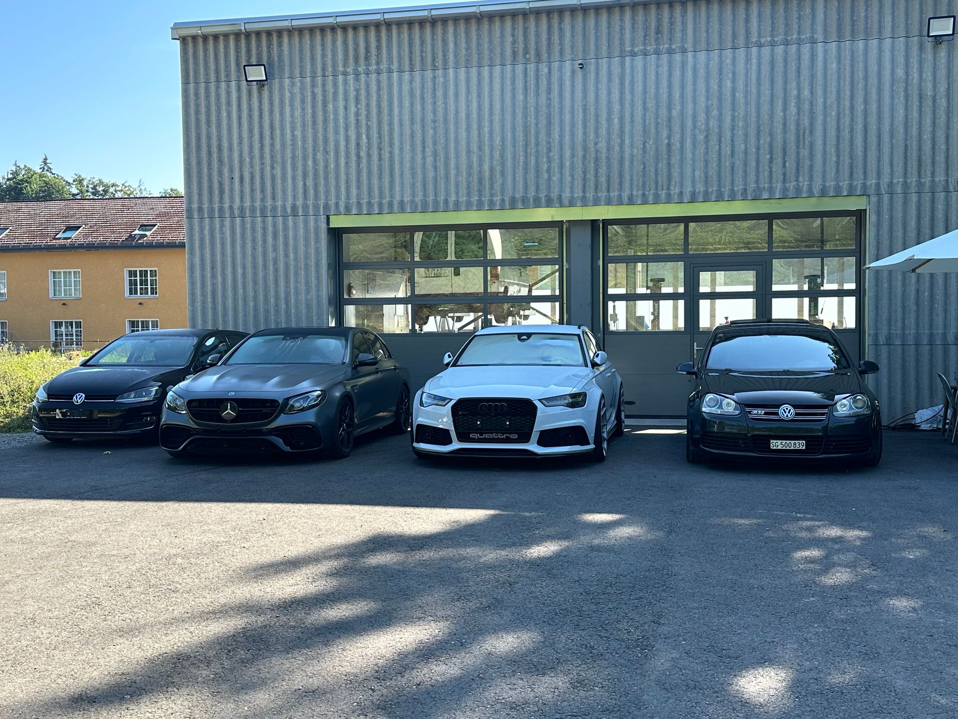 Four cars parked in front of a gray garage door on a sunny day.