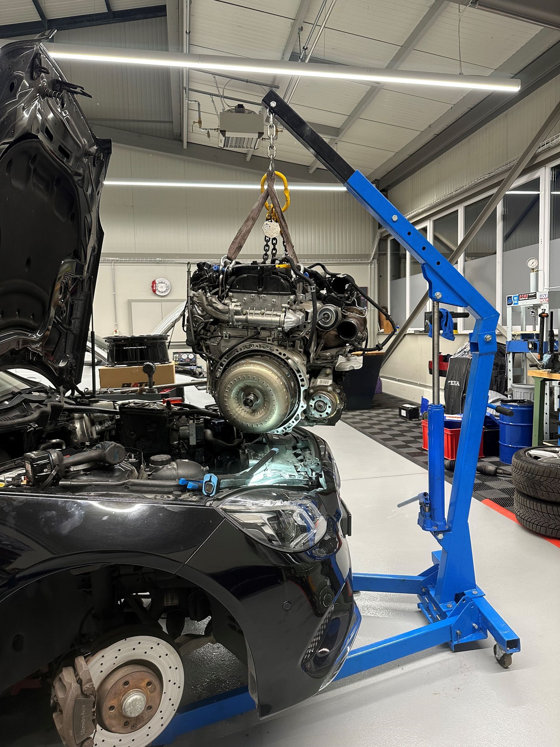 A car engine being lifted by a blue engine hoist inside a workshop.