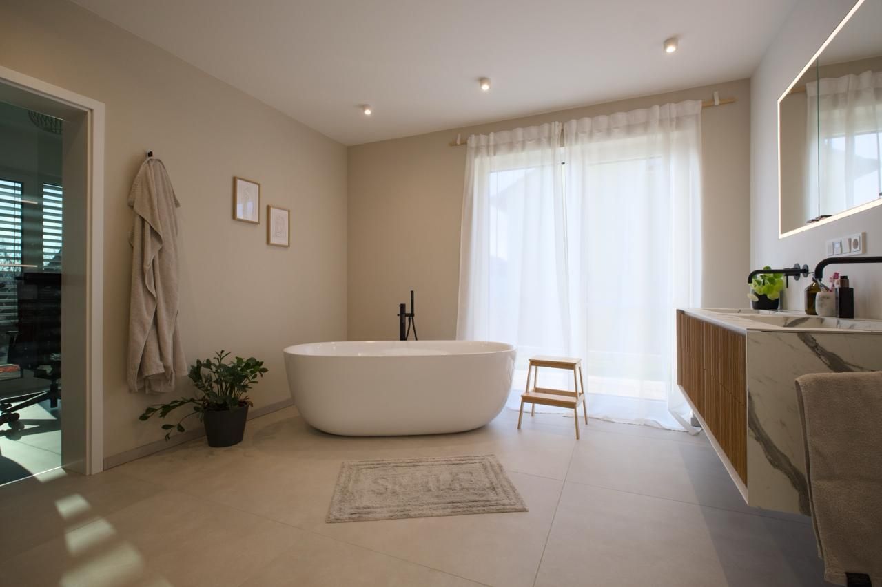 Minimalistisches Badezimmer mit freistehender Badewanne, transparenten Vorhängen, Waschtisch aus Holz und neutralen Beigetönen