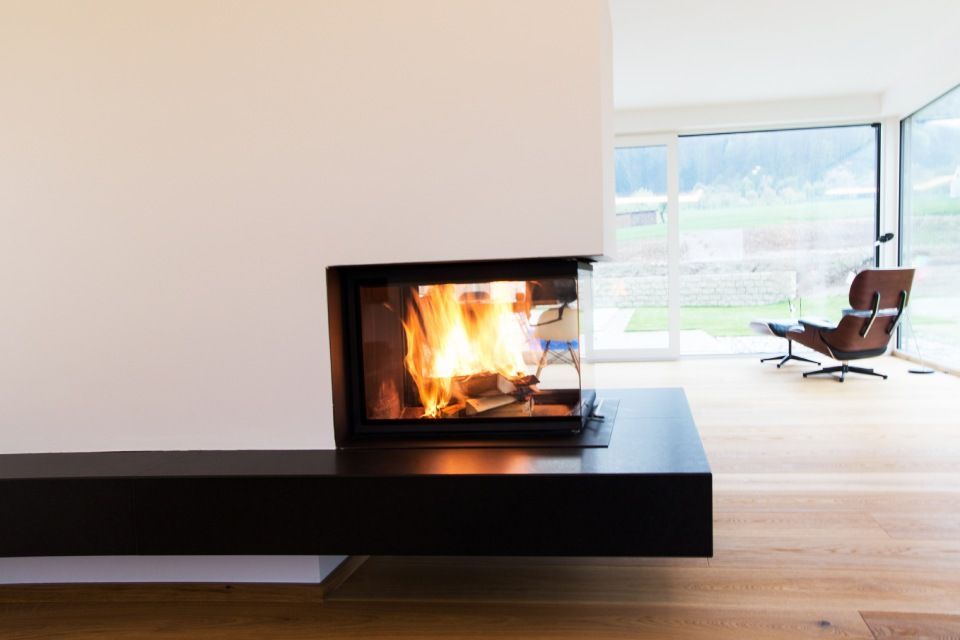 Modernes Wohnzimmer mit schwarzem Kamin und Feuerstelle, Holzboden und einem Sessel am großen Fenster.