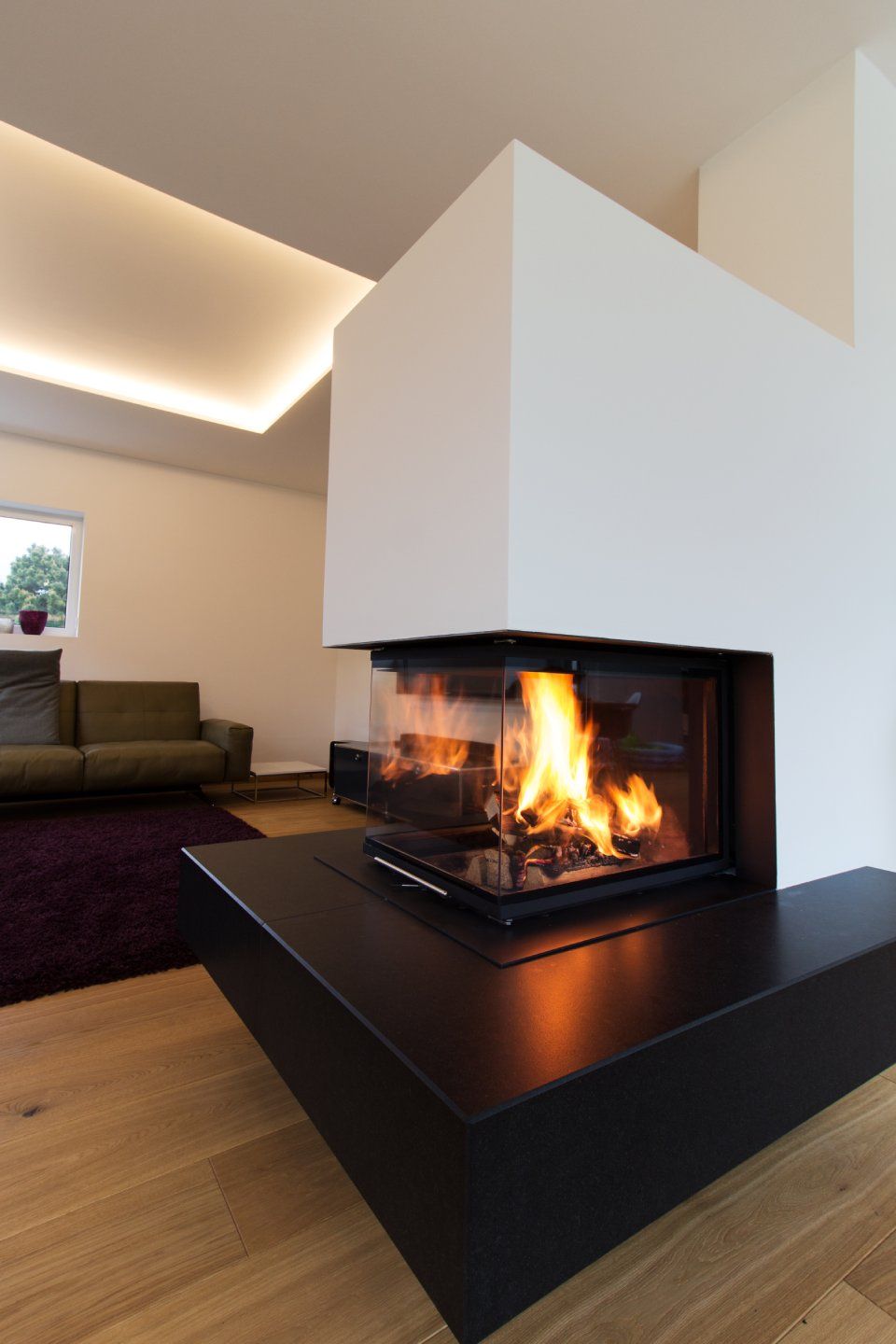 Modernes Wohnzimmer mit eingebautem Kamin und Flammen, schwarzem Kaminsims, Holzboden und Sofa im Hintergrund