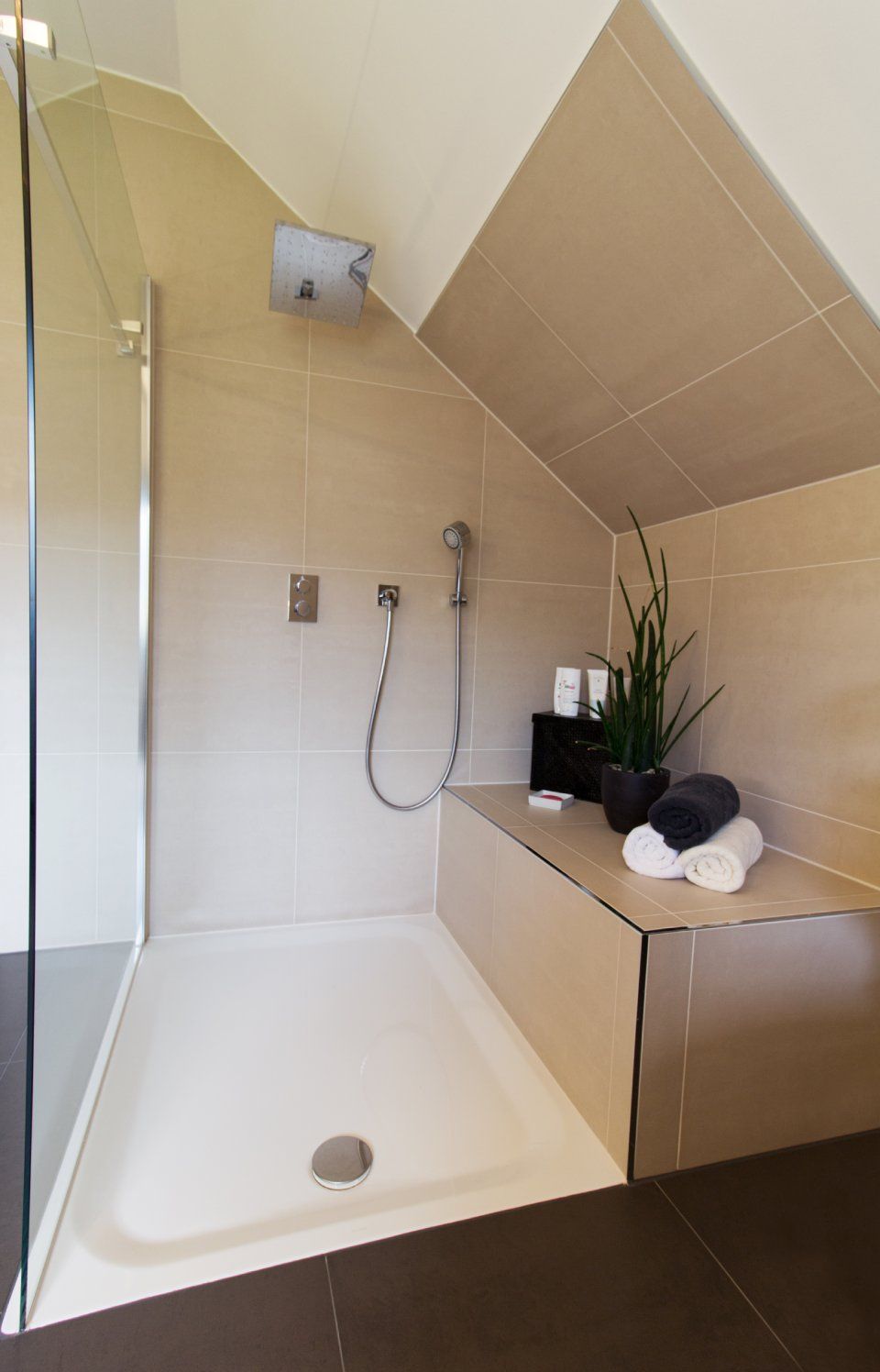 Moderne, ebenerdige Dusche mit beigefarbenen Fliesen, Glasabtrennung und Holzablage für Dekoration und Handtücher.