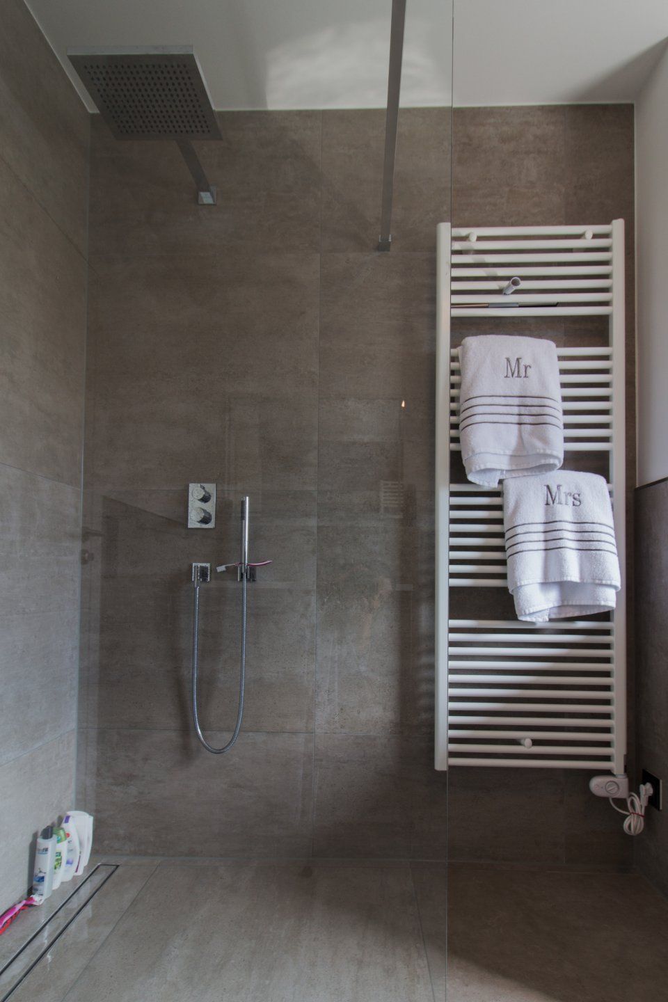Modernes Badezimmer mit Dusche, grauen Fliesen, Wandduschkopf und einem weißen Handtuchwärmer mit gefalteten Handtüchern.