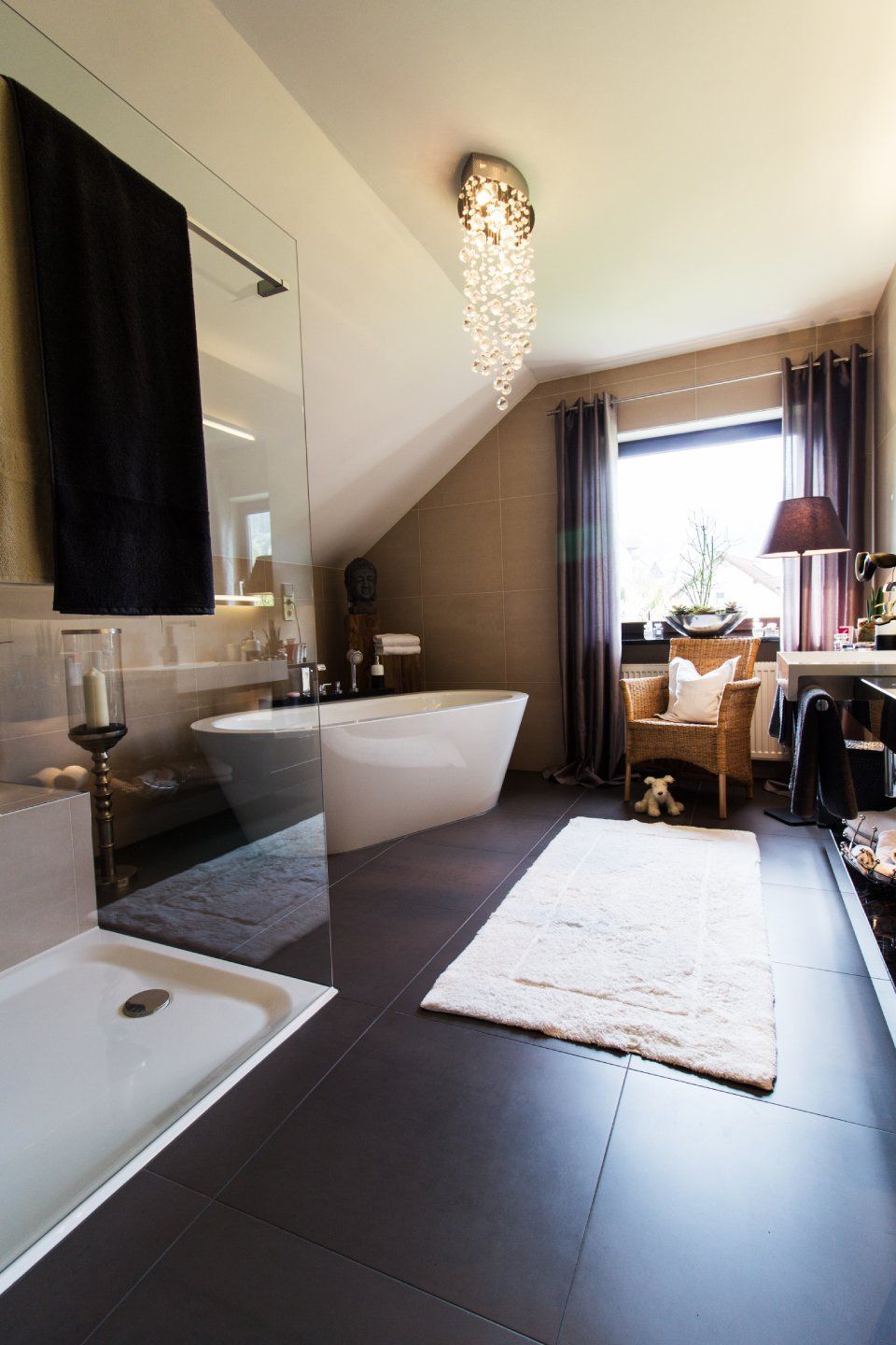Modernes Badezimmer mit freistehender Badewanne, dunklem Fliesenboden, Kronleuchter und Fensterbank am Fenster