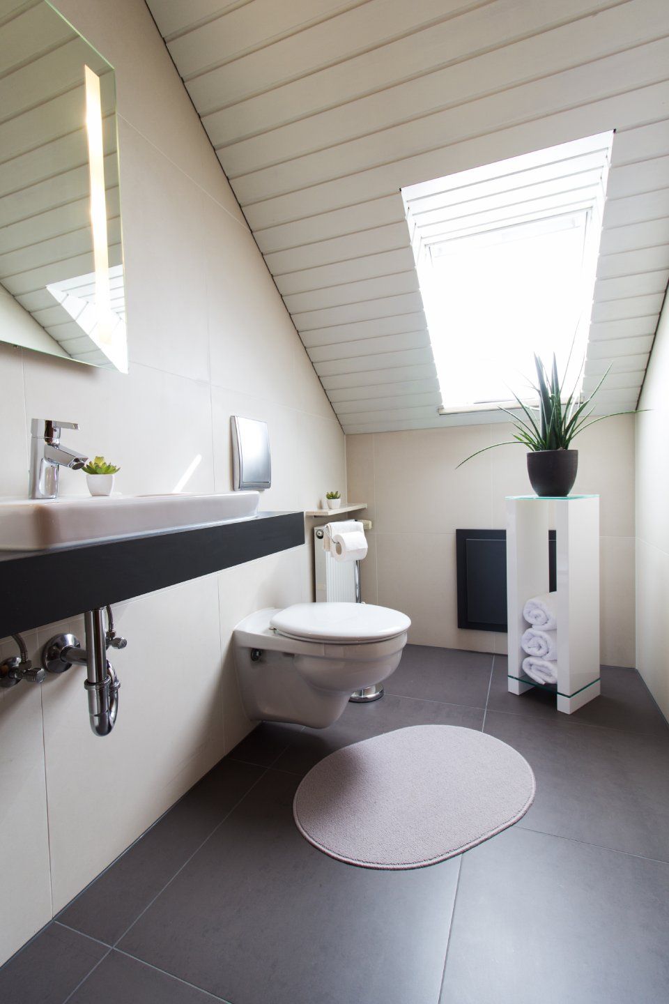 Modernes Badezimmer mit wandmontiertem Waschbecken, Toilette, Dachfenster, rundem Teppich und Topfpflanze