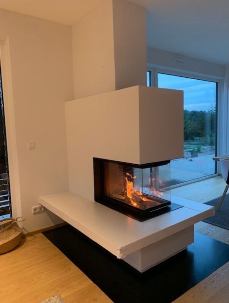 Moderner weißer Kamin mit gläsernem Feuerraum in einem hellen Wohnzimmer in der Nähe eines großen Fensters