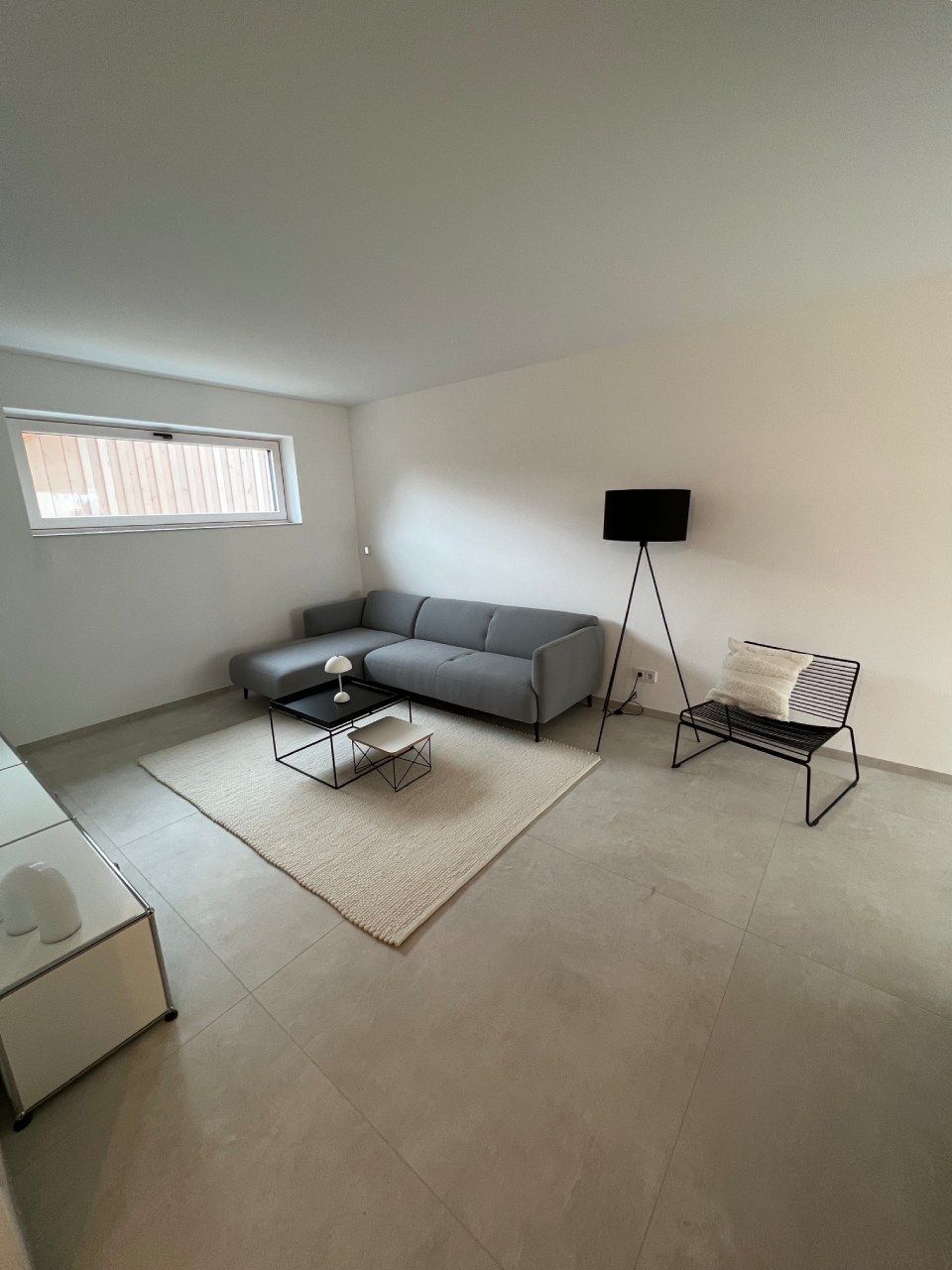 Minimalistisches Wohnzimmer mit grauem Ecksofa, Couchtisch, Stehlampe und Teppich
