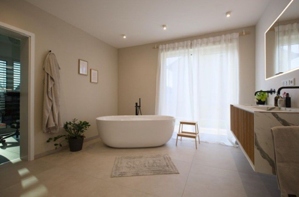 Minimalistisches Badezimmer mit freistehender Badewanne, transparenten Vorhängen, Waschtisch aus Holz und neutralen Beigetönen
