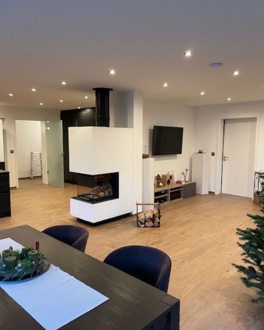 Modernes, offenes Wohnzimmer mit weißem Kamin, Fernseher, Esstisch und Einbauleuchten