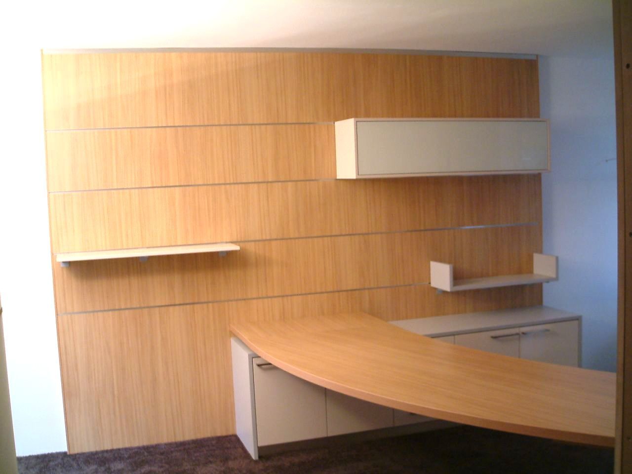 Verkleidete Wand mit Paneelen und eingebauten Schränken, Ablagen und einem abgerundetem Schreibtisch