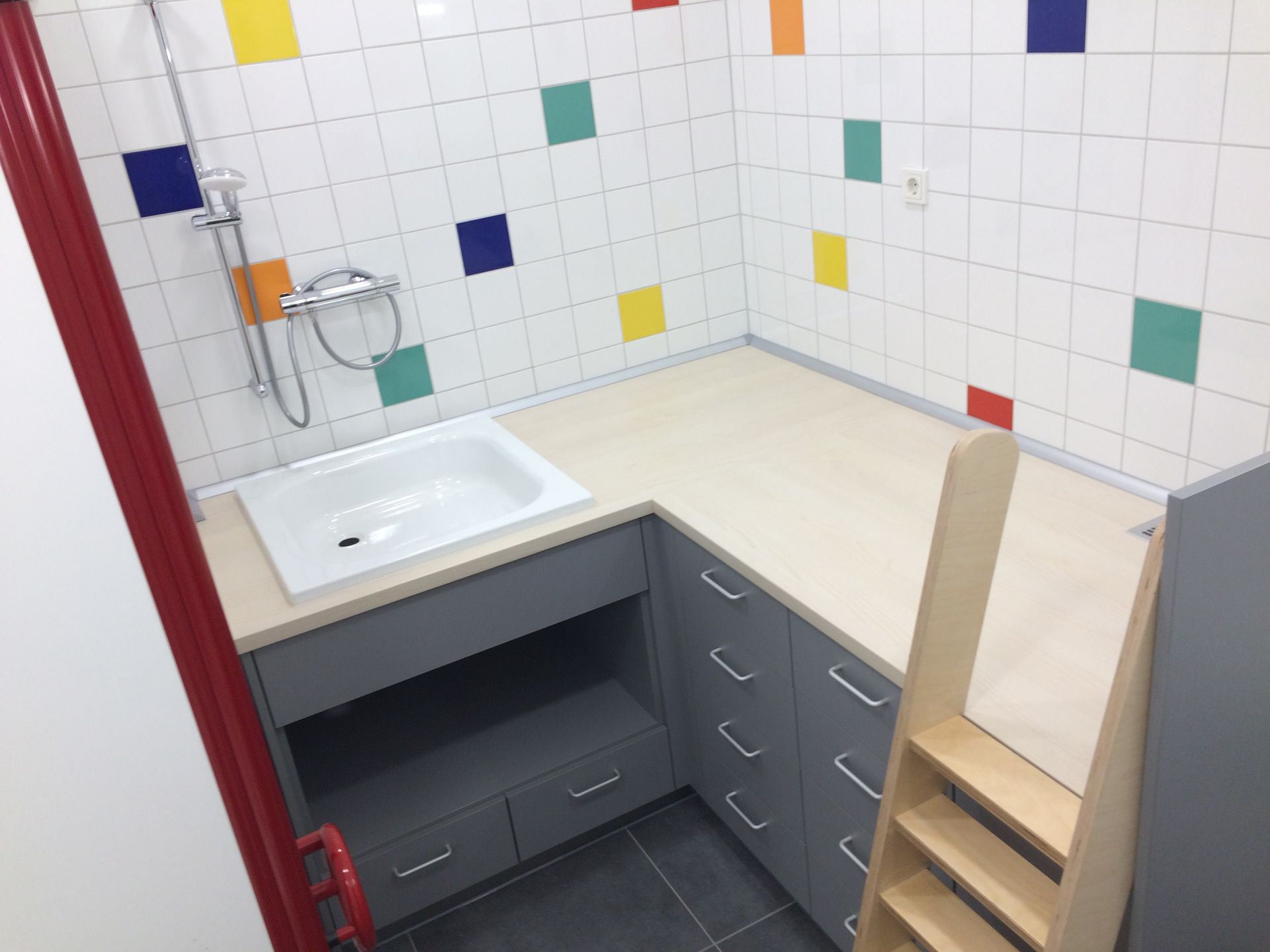 Wickelkommode im Kindergarten, mit Duschtasse und Treppe, Fronten in grau, Oberfläche helles Holz