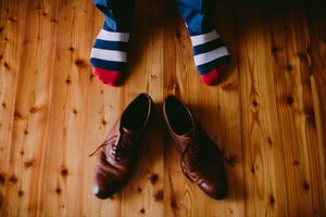 Una persona que lleva calcetines a rayas está de pie junto a un par de zapatos marrones sobre un piso de madera.