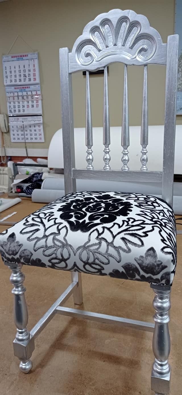 Una silla plateada con un cojín blanco y negro está sobre un piso de madera.