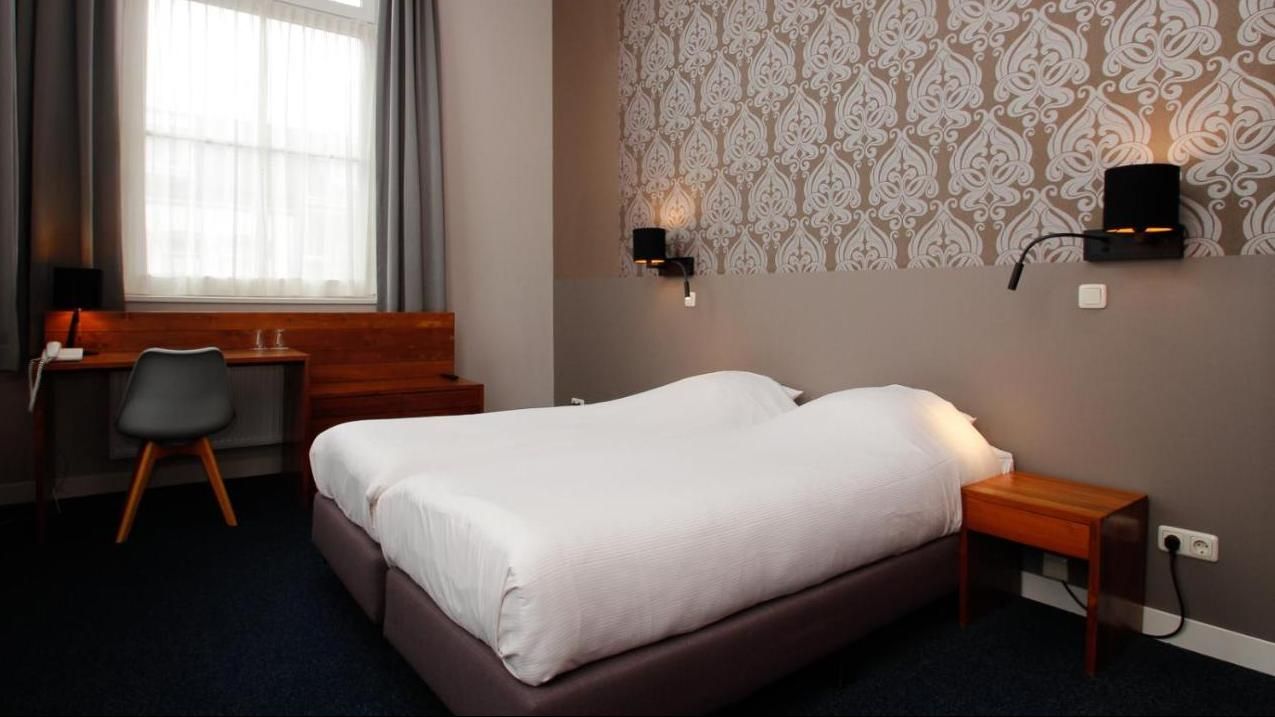 Een hotelkamer met twee bedden, een bureau en een raam.